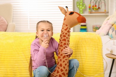 Photo of Little girl with toy giraffe and nebulizer for inhalation at home