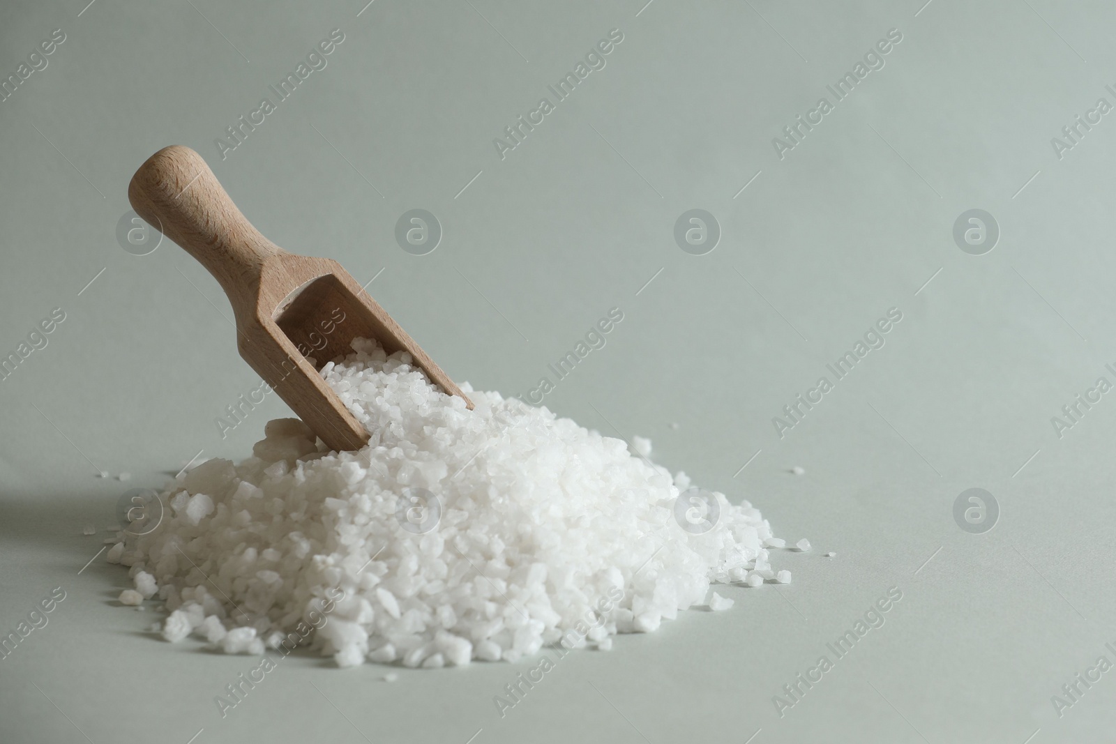 Photo of Organic salt and wooden scoop on light grey background. Space for text