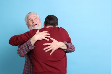 Photo of Happy dad and his son hugging on light blue background, space for text
