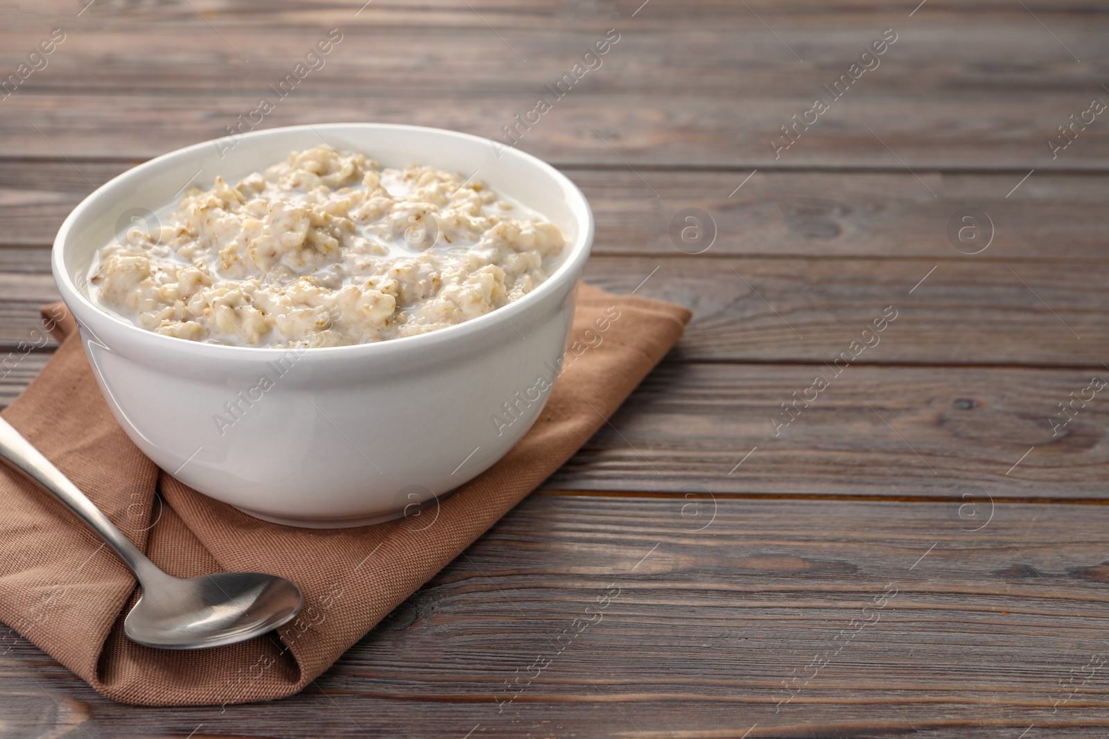 Photo of Tasty boiled oatmeal in bowl and spoon on wooden table, space for text