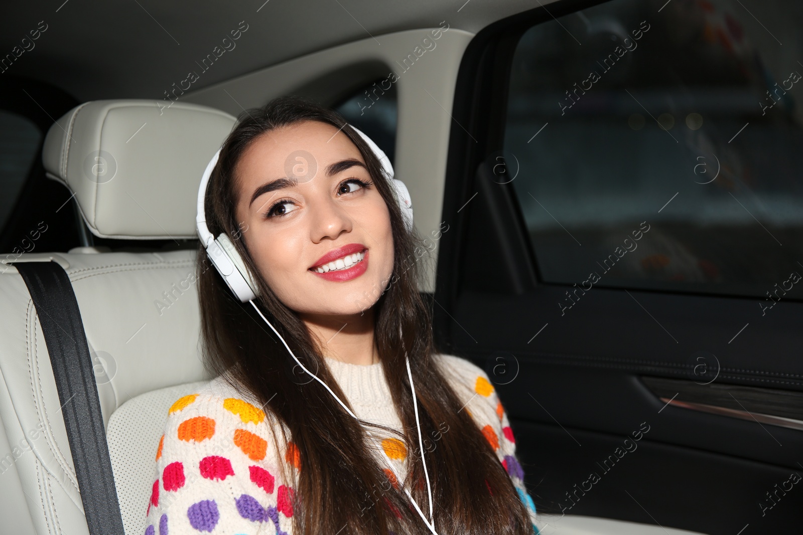 Photo of Beautiful young woman listening to music with headphones in car. Space for text