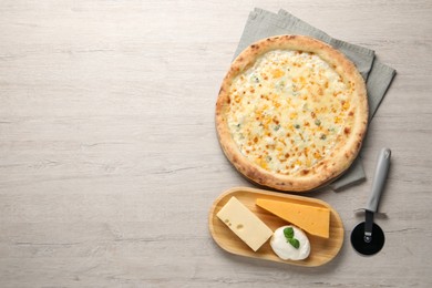 Photo of Delicious cheese pizza, cutter and different kinds of cheese on wooden table, flat lay. Space for text