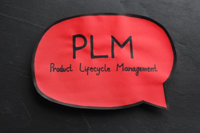 Paper speech bubble with abbreviation PLM (Product Lifecycle Management) on black slate background, top view