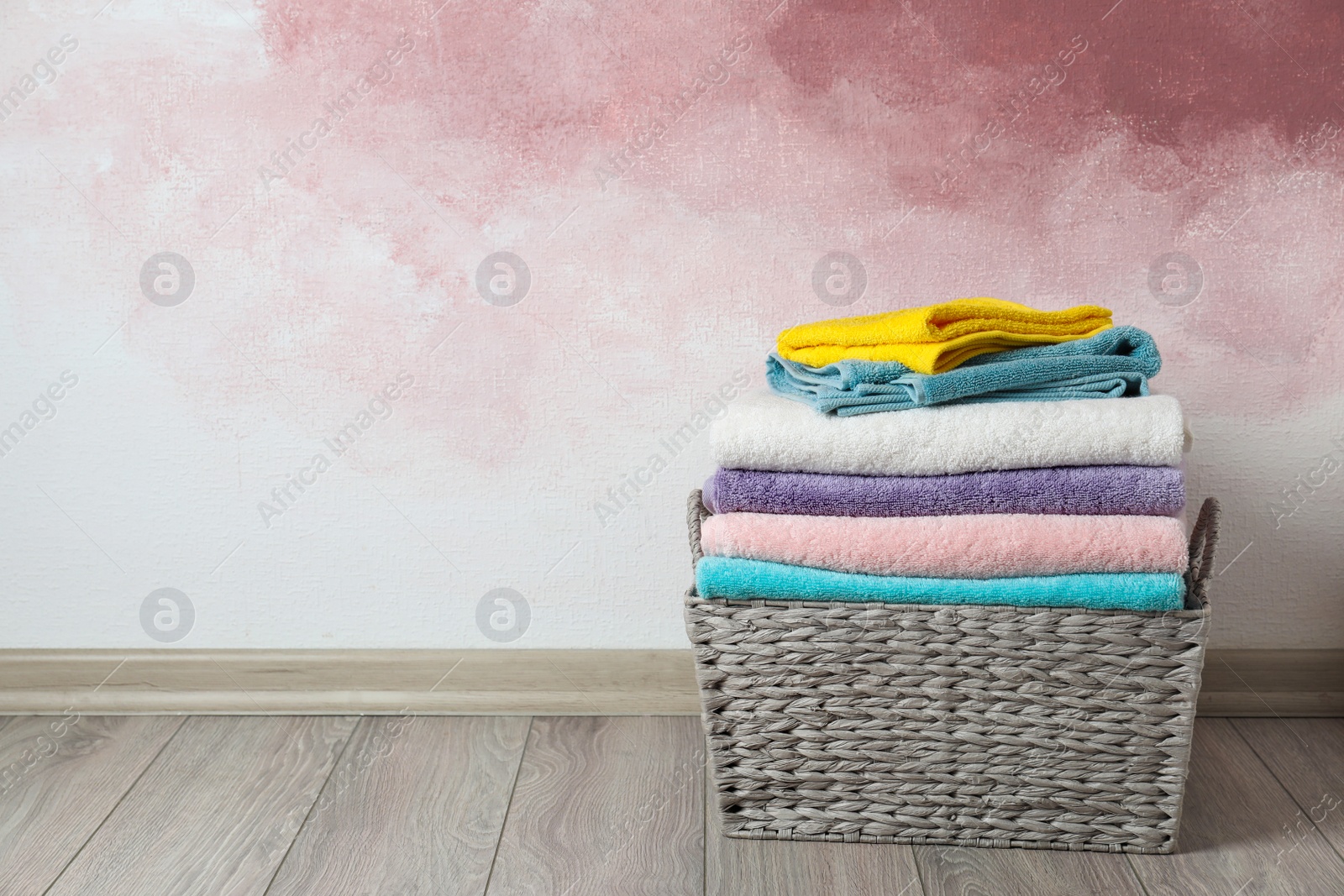 Photo of Basket with clean laundry on wooden floor near pink wall, space for text