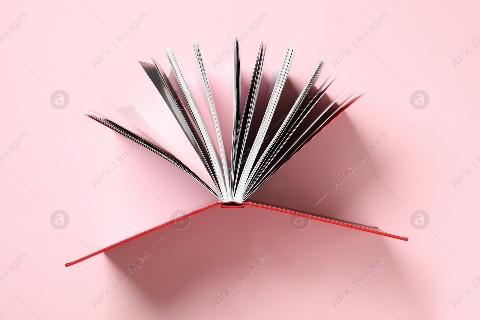 Photo of Open book with red cover on pink background, top view