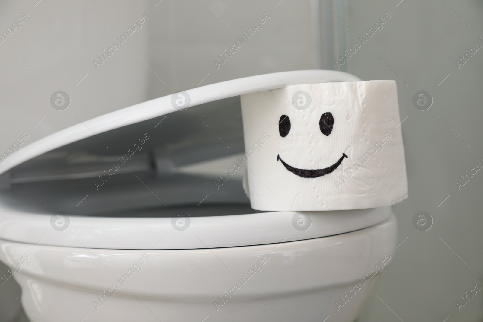 Photo of Roll of paper with drawn funny face on toilet seat in bathroom, closeup