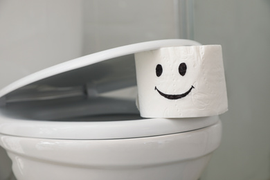 Photo of Roll of paper with drawn funny face on toilet seat in bathroom, closeup