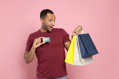 Photo of Happy African American man with shopping bags and credit card on pink background
