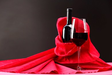 Photo of Stylish presentation of delicious red wine in bottle and glass on pink table against dark background. Space for text