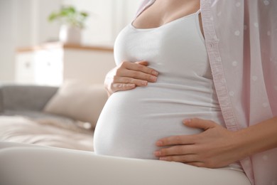 Photo of Pregnant woman touching her belly indoors, closeup