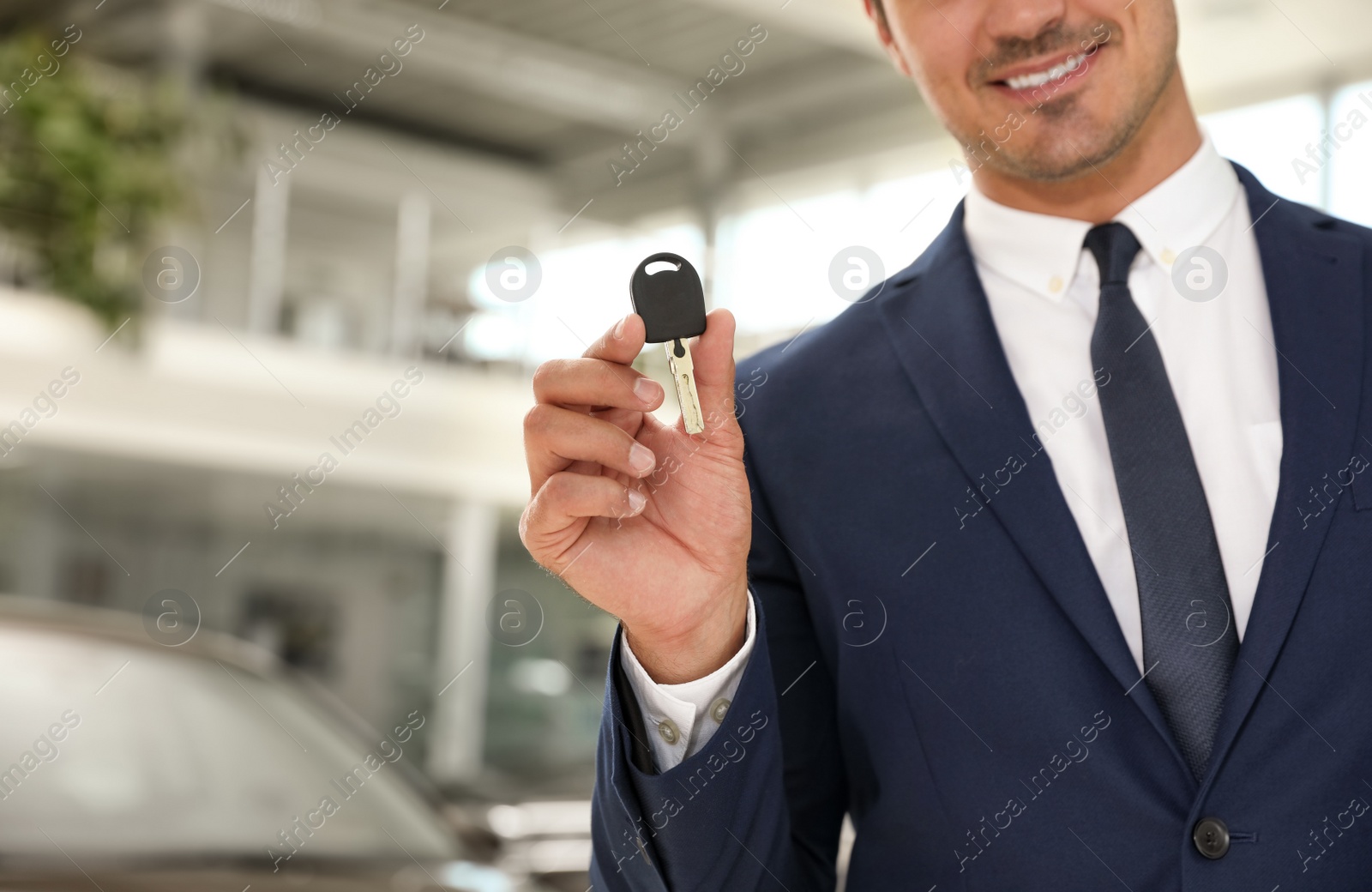 Photo of Young salesman with car key in modern dealership, focus on hand