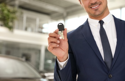 Young salesman with car key in modern dealership, focus on hand