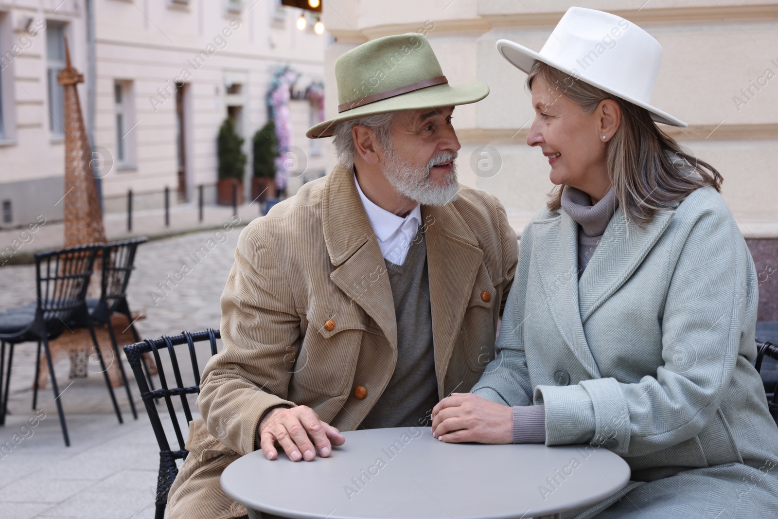 Photo of Portrait of affectionate senior couple sitting in outdoor cafe, space for text