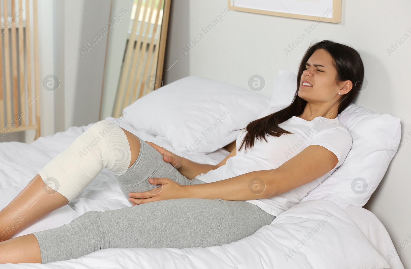 Photo of Young woman with leg wrapped in medical bandage in bedroom