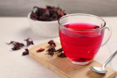 Cup of fresh hibiscus tea, dry flower leaves and spoon on wooden table. Space for text