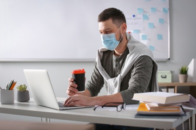 Teacher with protective mask conducting online lesson in classroom during COVID-19 quarantine