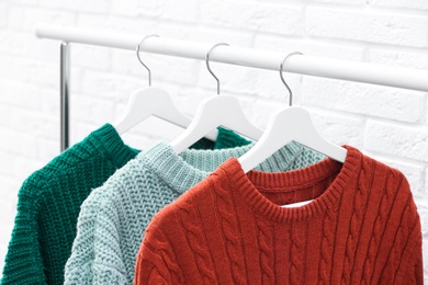 Collection of warm sweaters hanging on rack near brick wall