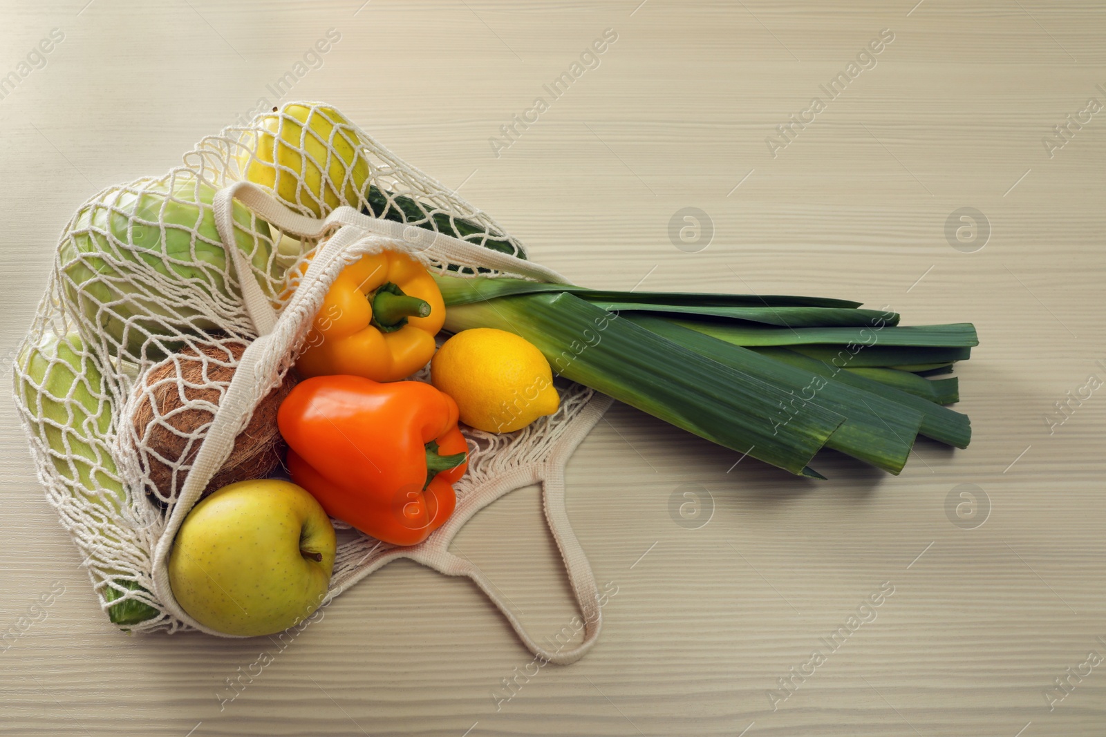 Photo of Net bag with vegetables and fruits on wooden table