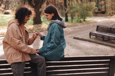 Happy young couple spending time together on wooden bench in autumn park, space for text. Dating agency