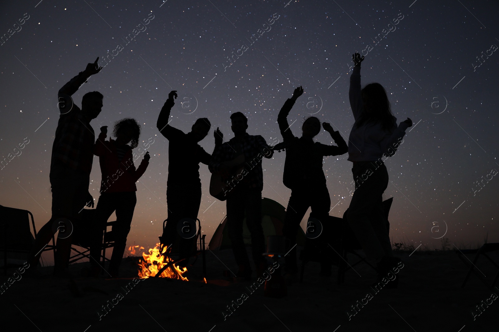 Photo of Group of friends having party near bonfire in evening. Camping season