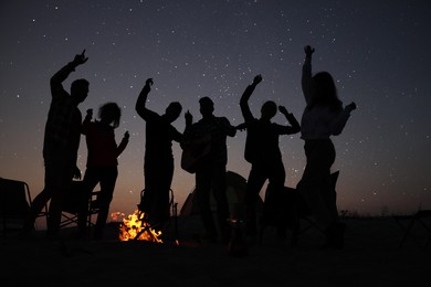 Photo of Group of friends having party near bonfire in evening. Camping season