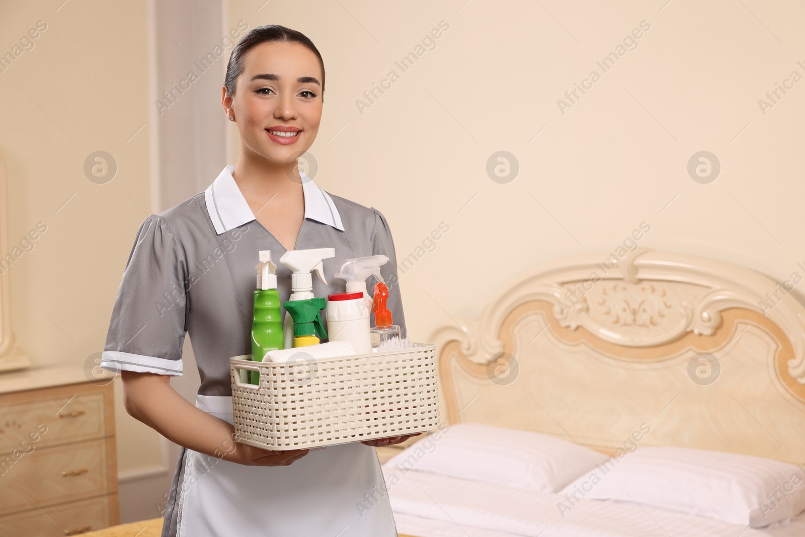 Photo of Young chambermaid holding basket with cleaning products in hotel room. Space for text