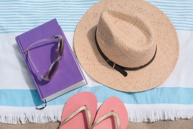 Photo of Beach towel with straw hat, book, sunglasses and flip flops on sand, flat lay