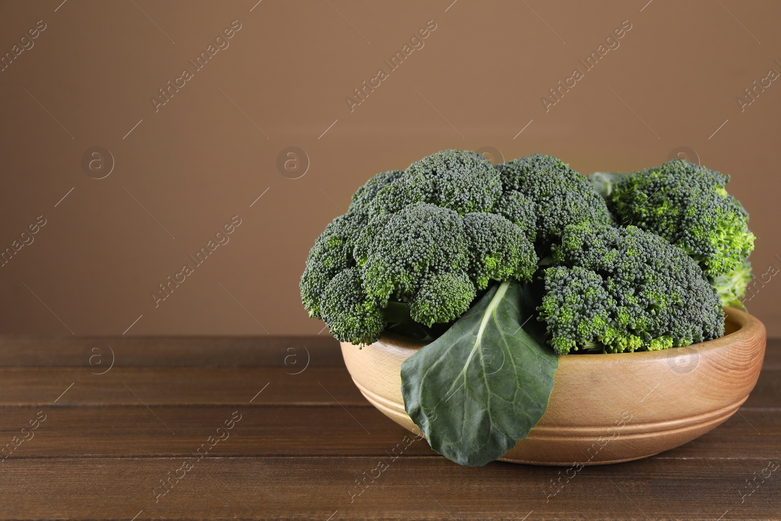 Photo of Bowl with fresh raw broccoli on wooden table, space for text