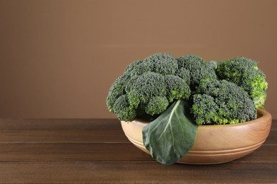 Bowl with fresh raw broccoli on wooden table, space for text