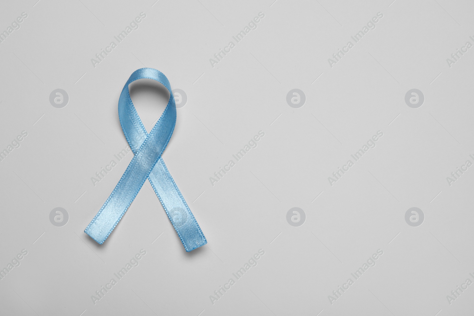 Photo of Light blue awareness ribbon on color background, top view. Space for text