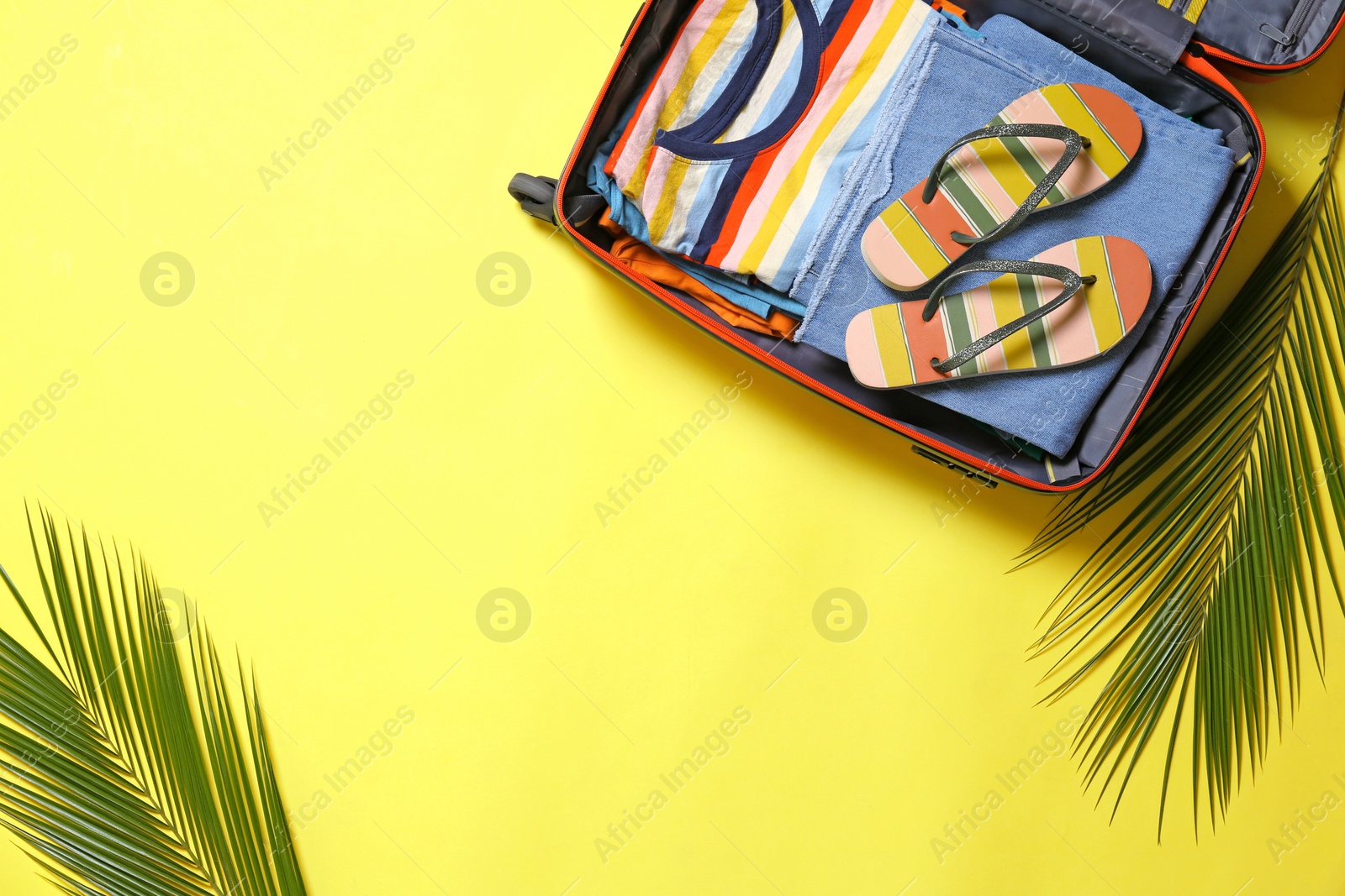Photo of Open suitcase and beach accessories on yellow background, flat lay. Space for text