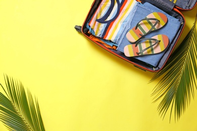 Open suitcase and beach accessories on yellow background, flat lay. Space for text