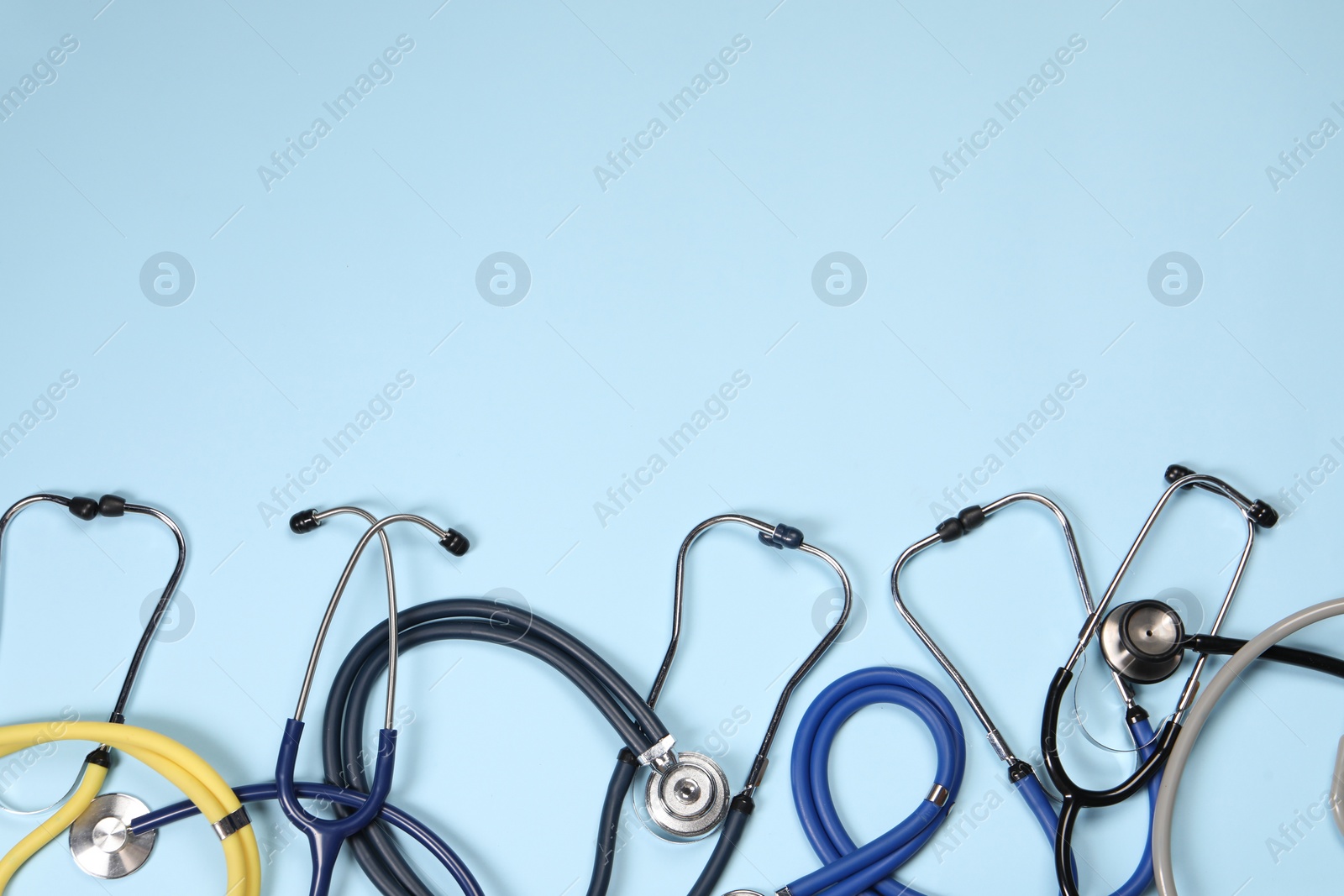 Photo of Stethoscopes on light blue background, flat lay. Space for text