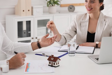 Photo of Real estate agent giving house key to young man in office, closeup. Mortgage concept