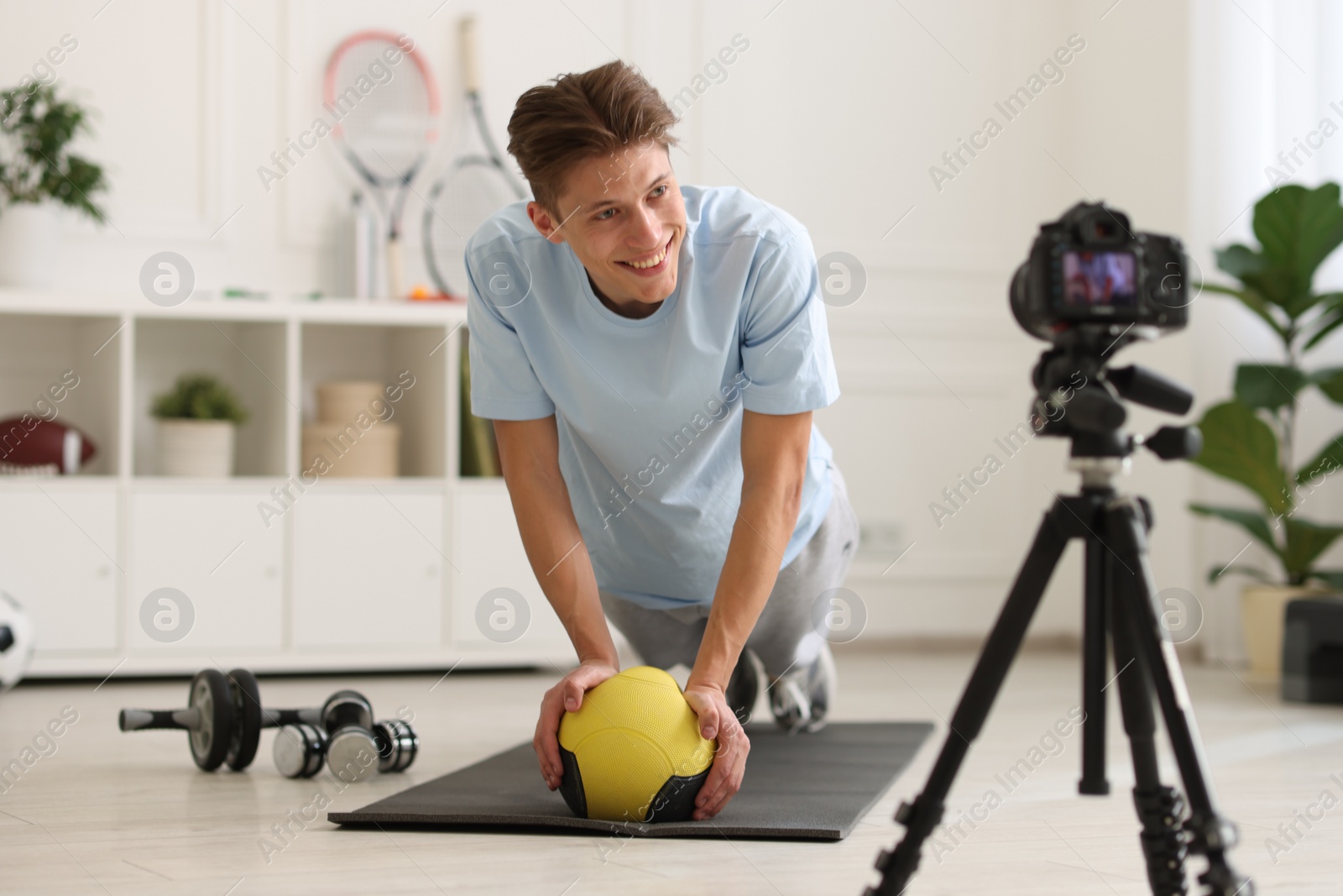 Photo of Smiling sports blogger training with medicine ball while recording fitness lesson with camera at home