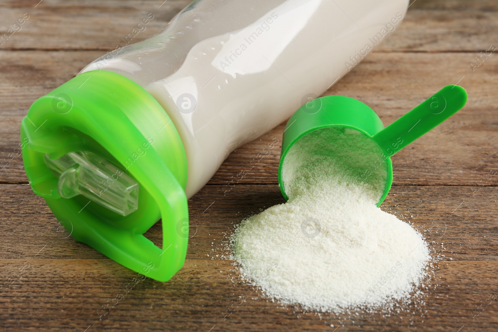 Photo of Measuring scoop of protein powder and bottle with shake on wooden table, closeup