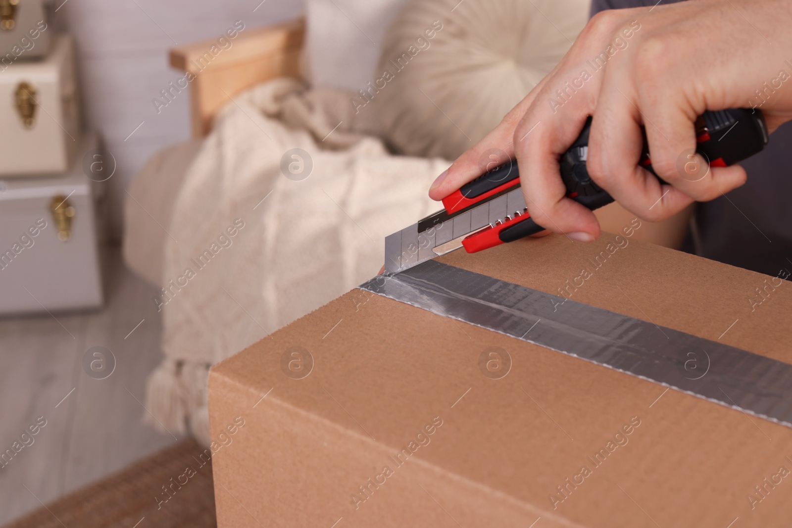 Photo of Man using utility knife to open parcel at home, closeup