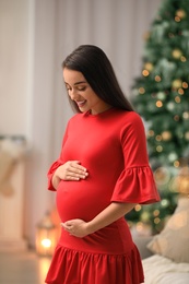 Happy pregnant woman in room decorated for Christmas. Expecting baby