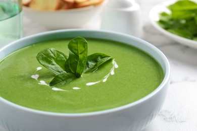 Photo of Bowl of healthy green soup with fresh spinach on marble table, closeup view