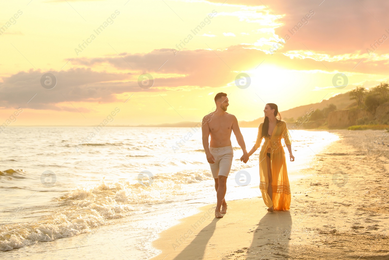 Photo of Happy young couple walking together on beach at sunset