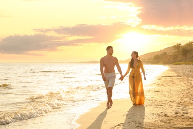 Happy young couple walking together on beach at sunset