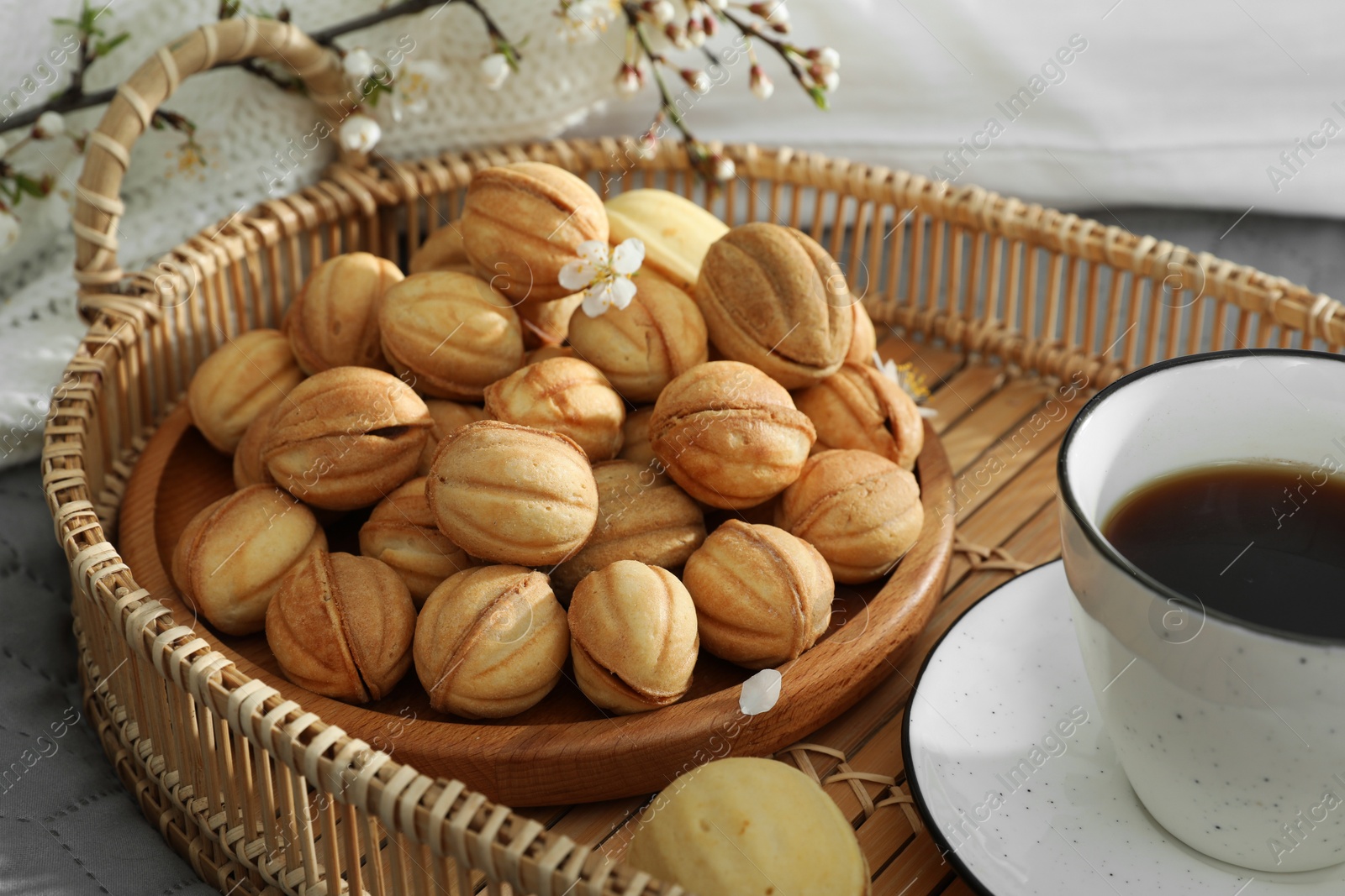 Photo of Delicious walnut shaped cookies with filling, cherry branch and cup of coffee on grey blanket, closeup. Homemade popular biscuits from childhood