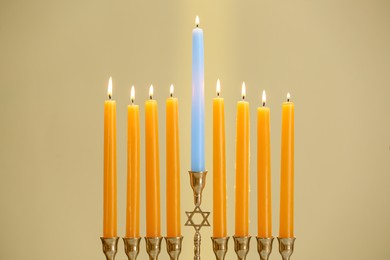 Photo of Hanukkah celebration. Menorah with burning candles on beige background, closeup