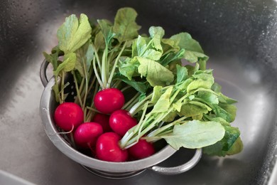 Photo of Fresh wet radishes in metal colander inside sink