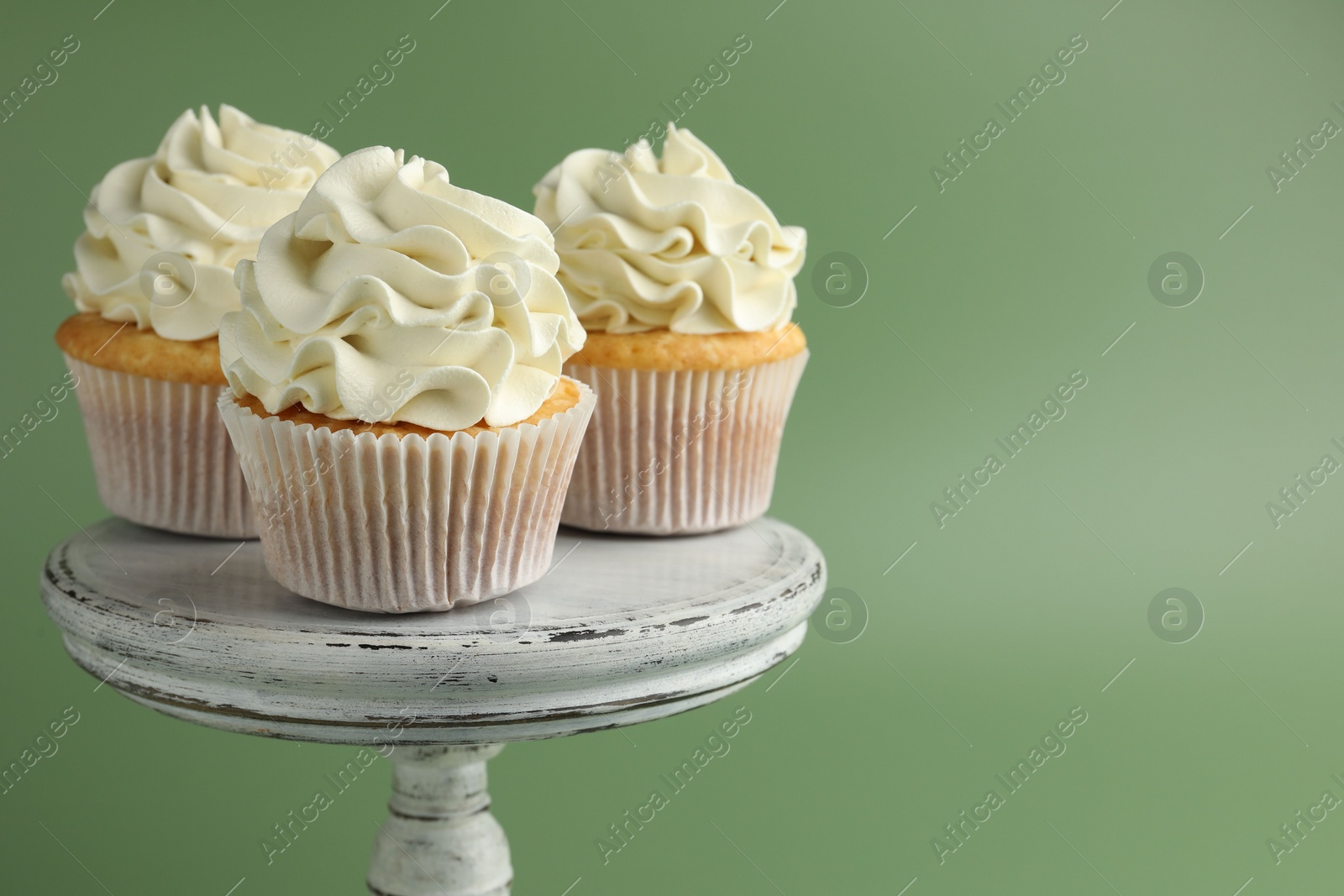 Photo of Tasty vanilla cupcakes with cream on green background, space for text