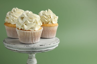 Tasty vanilla cupcakes with cream on green background, space for text