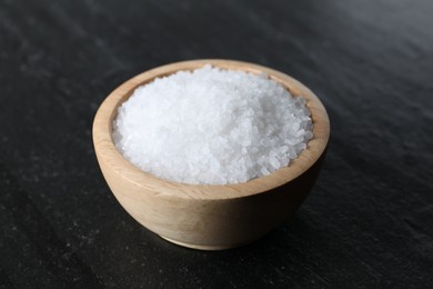 Photo of Organic white salt in bowl on black table, closeup