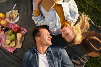 Happy young couple resting while having picnic outdoors on sunny day, top view