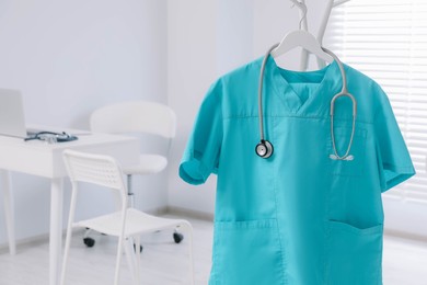 Photo of Turquoise medical uniform and stethoscope on rack in clinic. Space for text