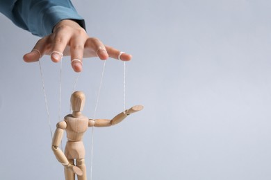 Photo of Woman pulling strings of puppet on light grey background, closeup. Space for text